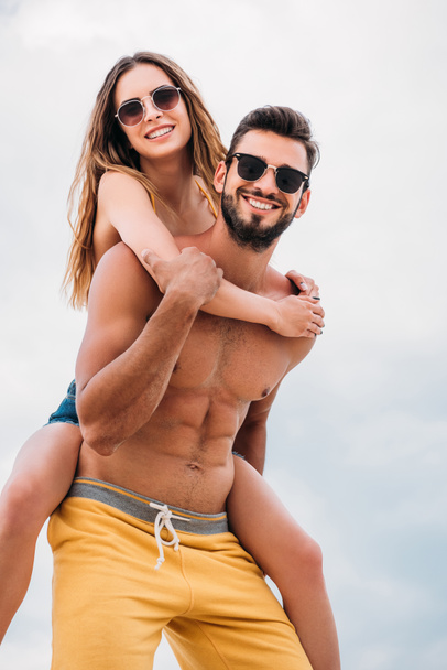 happy young woman piggybacking on boyfriends back in front of cloudy sky - 写真・画像