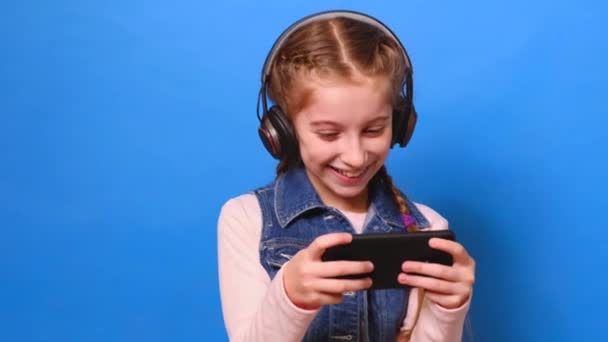 Young girl in headphones playing the video game on her smartphone - Filmagem, Vídeo