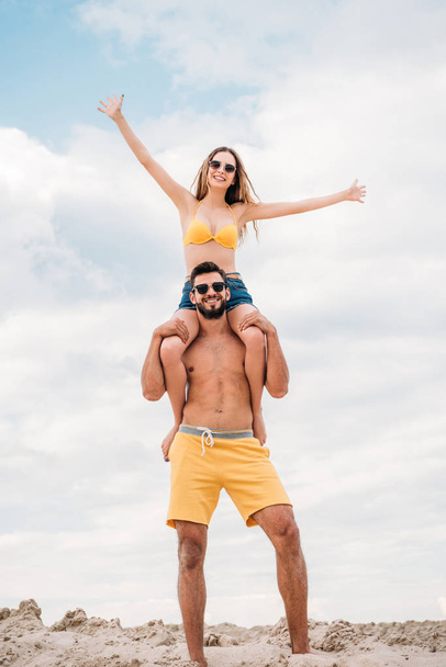 beautiful young woman riding on shoulders of boyfriend in front of cloudy sky - Foto, afbeelding