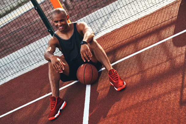 African sportsman sitting on arena court with ball - Foto, Bild