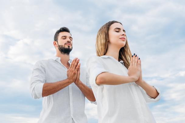 bottom view of young couple making namaste mudra against cloudy sky - Фото, изображение