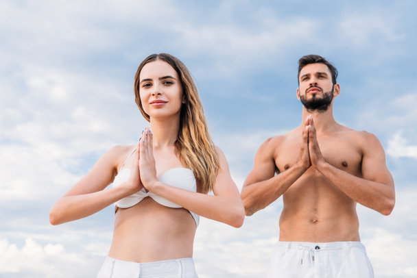 junges Paar macht Namaste Mudra und praktiziert Yoga vor bewölktem Himmel - Foto, Bild