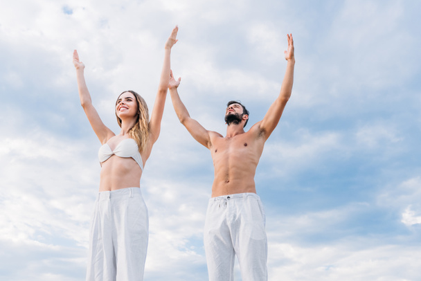 fit young couple with raised arms meditating under cloudy sky - Foto, Imagem