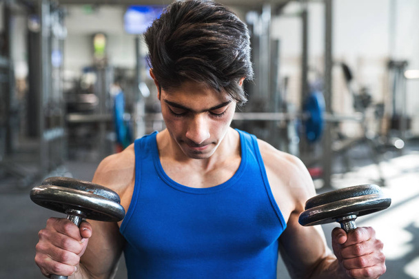 Young fit hispanic man in gym exercising with dumbbells. - Foto, Bild