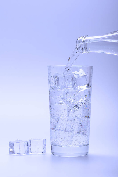 Despeje água doce em um copo com gelo de uma garrafa. Cubos de gelo ao lado de um copo
. - Foto, Imagem