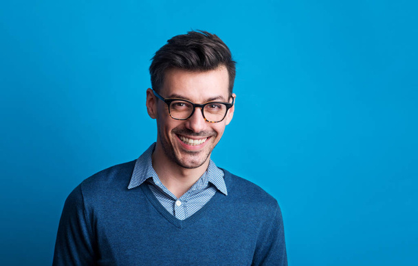 Portrait of a young man with glasses in a studio on a blue background. - Фото, изображение