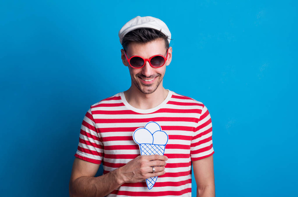 Portrait of a young man in a studio with sunglasses on a blue background. - Foto, afbeelding