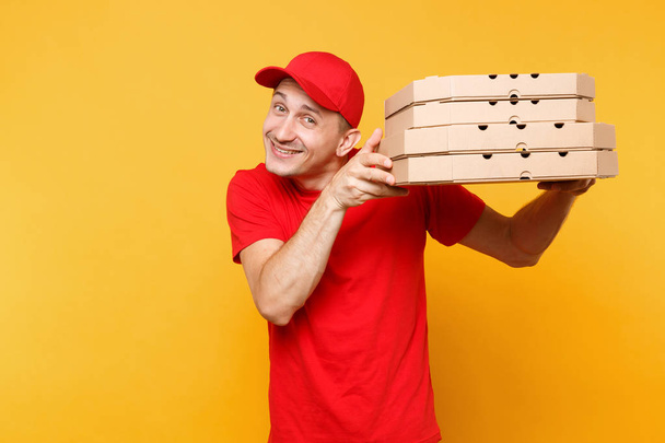 Repartidor en gorra roja, camiseta con cajas de pizza para pedidos de comida aisladas sobre fondo amarillo. Hombre empleado pizzaman o courier en uniforme sosteniendo pizza italiana en caja plana de cartón. Concepto de servicio
 - Foto, Imagen