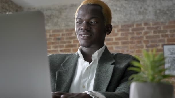 Young african blonde businessman typing on laptop and sitting in modern office, confident, laughing - Video