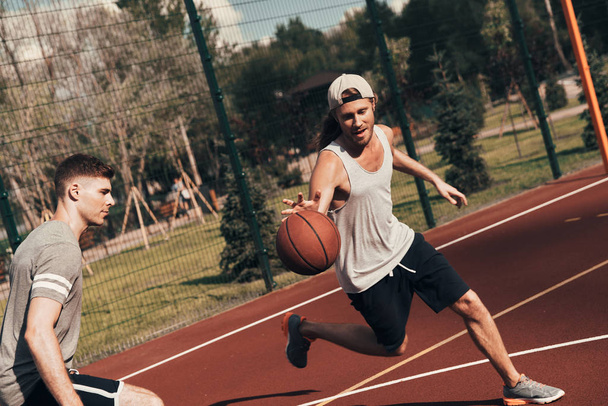 Pushing hard. Two young men in sports clothing playing basketball while spending time outdoors - Foto, Imagen