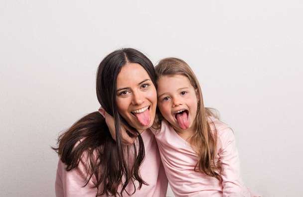 Ένα μικρό κορίτσι και τη μητέρα της να κολλήσει τη γλώσσα έξω σε ένα στούντιο. - Φωτογραφία, εικόνα