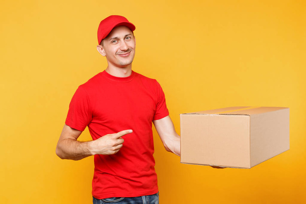 Delivery man in red uniform isolated on yellow orange background. Professional male employee courier or dealer in cap t-shirt holding empty cardboard box. Receiving package service concept. - Foto, Imagem