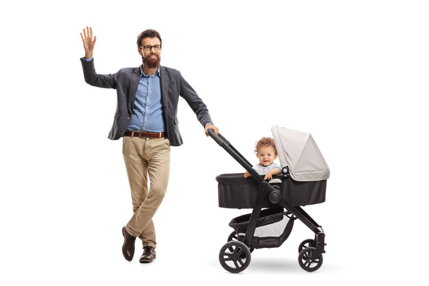Full length portrait of a father with a baby boy in a stroller waving at the camera isolated on white background - 写真・画像