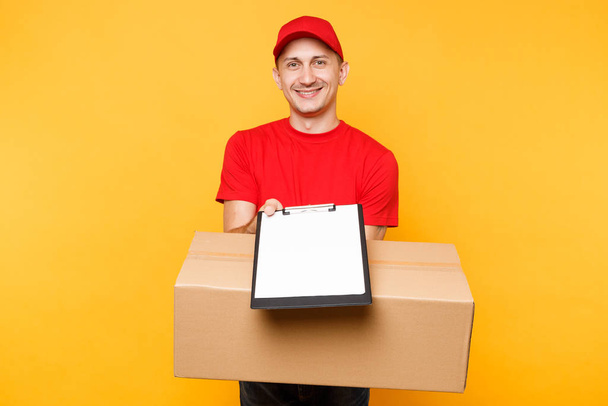 Delivery man in red uniform isolated on yellow background. Male employee courier in cap t-shirt hold pen clipboard with papers document blank empty sheet, cardboard box. Receiving package. Copy space - Photo, image