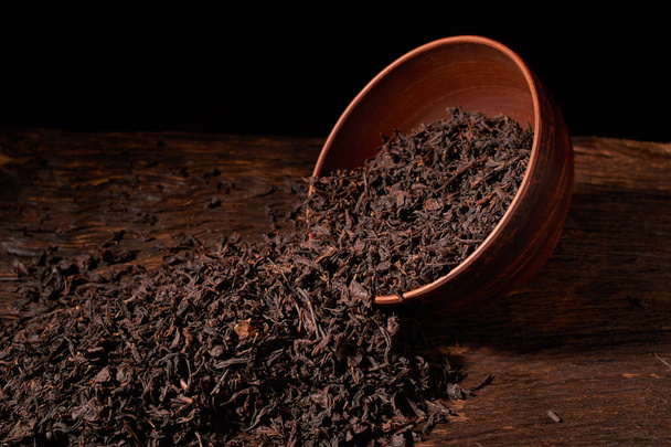 Pohled shora sušeného černého čaje v hliněné misky na dřevěný stůl. Koncept výroby čaje - Fotografie, Obrázek