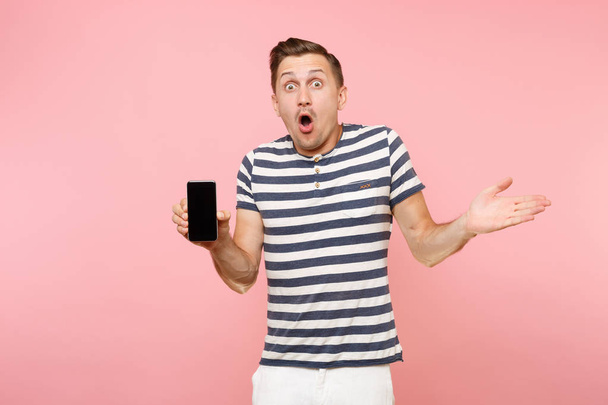 Porträt eines Mannes in gestreiftem T-Shirt, der eine Handykamera mit leeren schwarzen Bildschirmkopien zeigt, isoliert auf einem Trend-Pastellrosa-Hintergrund. Menschen aufrichtige Emotionen Konzept. Werbefläche - Foto, Bild