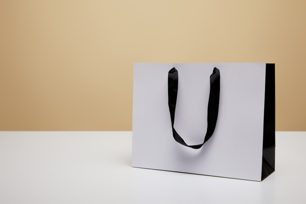 one white shopping bag on white table isolated on beige - Fotó, kép