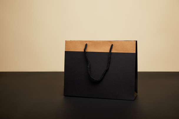 one black shopping bag on black table isolated on beige - Фото, изображение