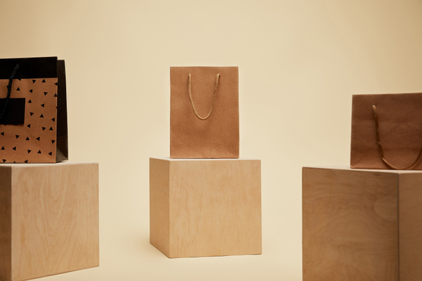 three paper shopping bags on wooden cubes isolated on beige  - Φωτογραφία, εικόνα