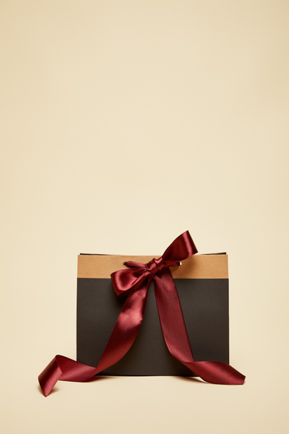 fashionable black shopping bag with burgundy bow isolated on beige - 写真・画像