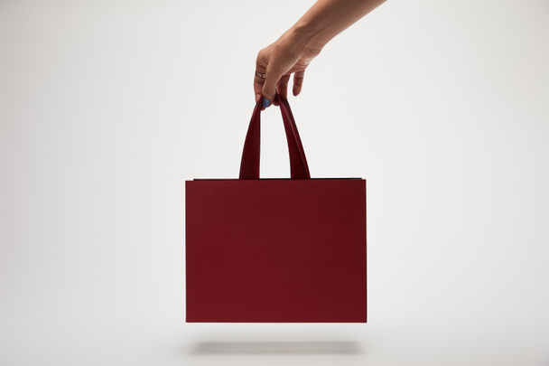 cropped image of woman holding burgundy shopping bag in hand isolated on white  - Photo, Image