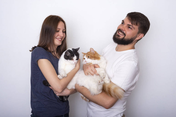 Happy young couple with their well-groomed cats poses in studio on a light background  - Фото, зображення