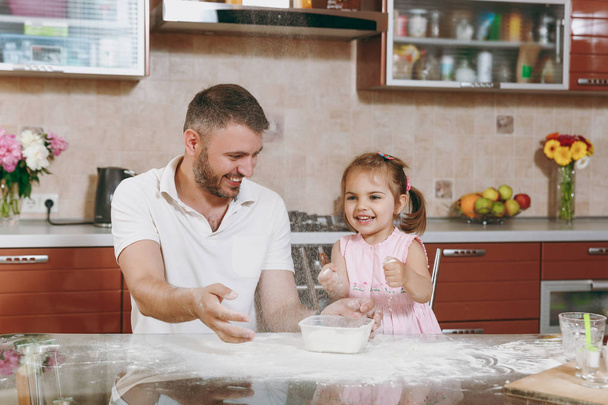 Little kid girl helps man to cook Christmas ginger cookies, playing with flour at table. Happy family dad, child daughter cooking food in weekend morning. Father's day holiday. Parenthood, childhood - Photo, Image