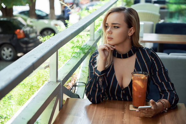 Taze içki holding ile bir kafede oturan düşünceli kadın bir  - Fotoğraf, Görsel