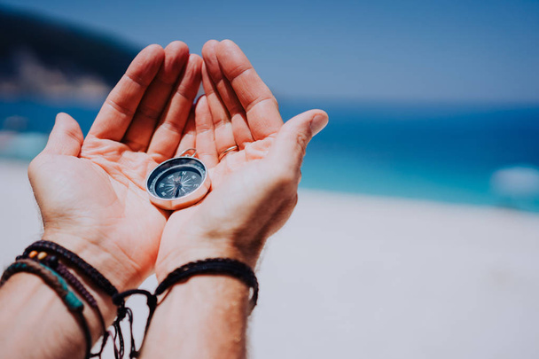 Open hand palms with metal compass on the sandy beach. Searching your way concept. Blue sea in background. Point of view pov - Φωτογραφία, εικόνα