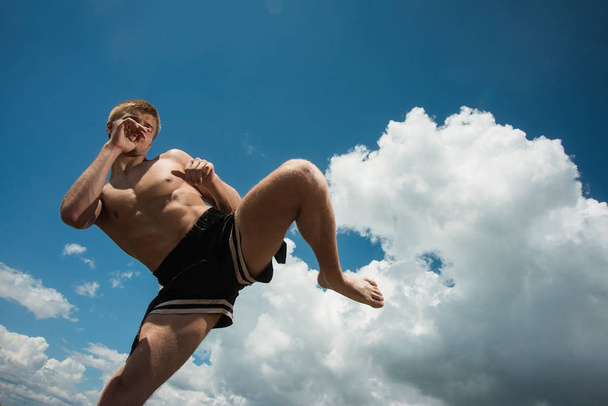 Kickboxer kicks in the open air in summer against the sea. - Φωτογραφία, εικόνα