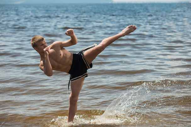 Kickboxer kicks in the open air in summer against the sea. - 写真・画像