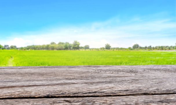 Vintage-Holztisch vor grünem Reisfeld oder Graslandhintergrund mit hellblauem Himmel zur Produktpräsentation - Foto, Bild