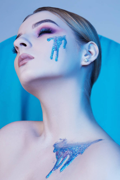 όμορφη νεαρή γυναίκα με μακιγιάζ και μπλε υγρό σχολιάζει σχετικά με την τέχνη της skin.body και συνθέτουν έννοια - Φωτογραφία, εικόνα