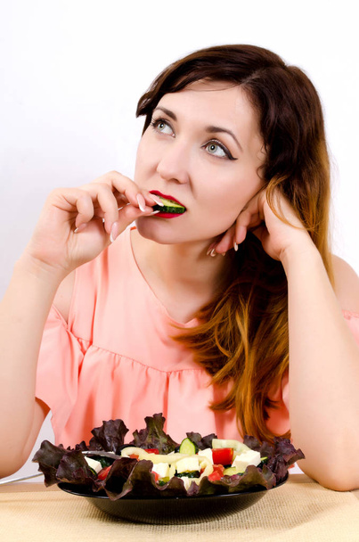 Egy fiatal nő eszik a salátát, és harap egy uborkát, miközben ő álmodik, fogyás, és egy szép szám - Fotó, kép