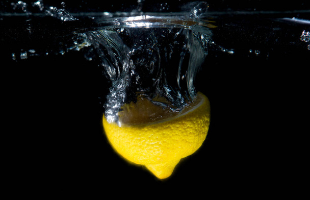 Lemon in water. Citrus fruit thrown into the water. - Photo, Image