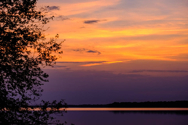 coucher de soleil coloré au bord du lac avec des silhouettes d'arbres et un ciel rouge en arrière-plan
 - Photo, image