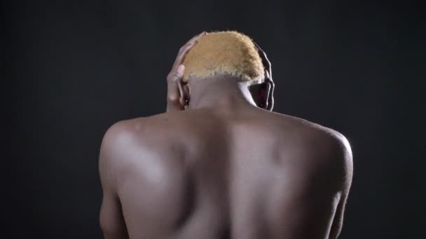 Naakt achterkant Afrikaanse jongeman die betrekking hebben op zijn oren, staan, geïsoleerd op zwarte achtergrond - Video