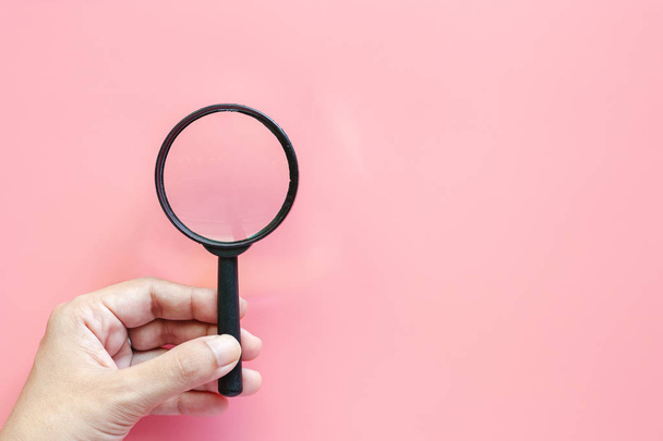 Hand holding a magnifying glass on pink background with copy space - Photo, Image