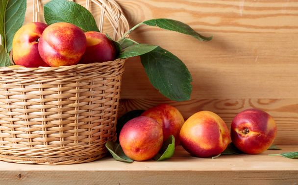Nectarines with leaves in a wicker basket on a wooden table. - Photo, Image