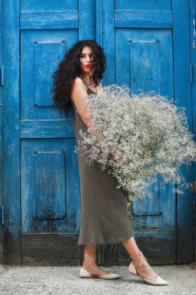la ragazza si trova vicino alla porta blu con un grande mazzo di fiori selvatici
 - Foto, immagini