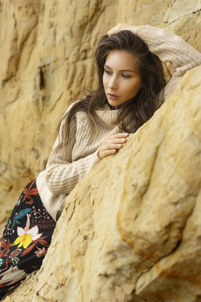 Beautiful girl wearing a beige sweater and a black skirt with a pattern in the form of large flowers posing in a sandy quarry. Advertising, lifestyle, fashion and commercial design. Copy space. - 写真・画像