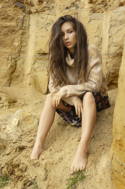 Beautiful girl wearing a beige sweater and a black skirt with a pattern in the form of large flowers posing in a sandy quarry. Advertising, lifestyle, fashion and commercial design. Copy space. - Foto, Imagen
