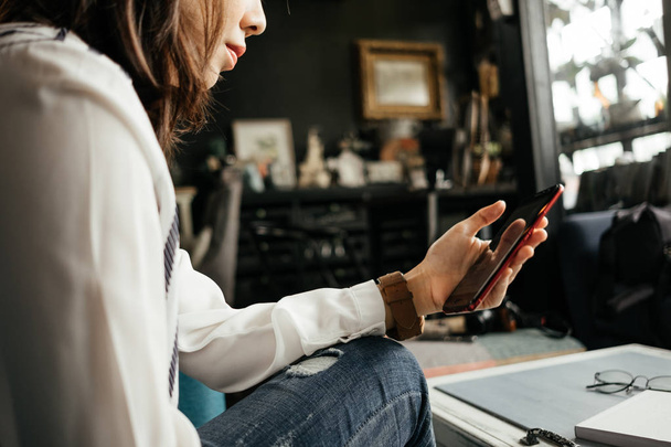 молодая деловая женщина, сидящая на рабочем месте и с помощью мобильного телефона имеет ноутбук и очки на фоне стола
 - Фото, изображение