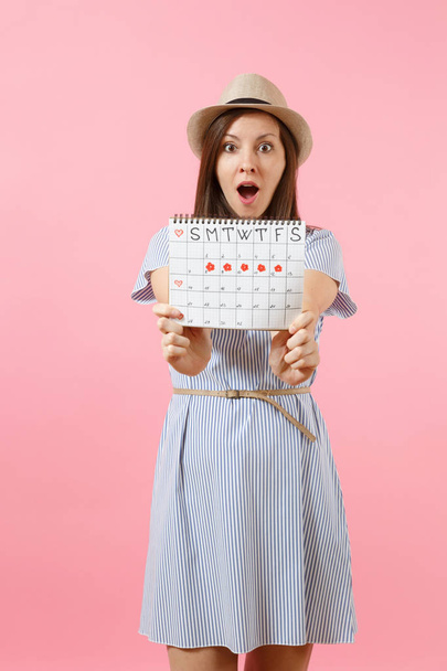 Портрет молодої жінки в блакитній сукні, капелюх тримає календар на перевірку менструальних днів ізольовано на яскравому тлі рожевого кольору. Медична, охорона здоров'я, гінекологічна концепція. Копіювати простір
 - Фото, зображення