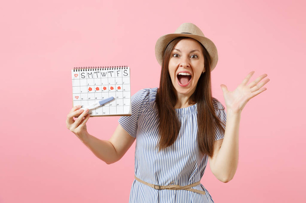 Nadšený, šťastná žena v modrých šatech, klobouk drží v ruce těhotenský test, období kalendáře pro kontrolu dní menstruace izolované na růžovém pozadí. Lékařské, zdravotnické, gynekologické koncept. Kopírovat prostor - Fotografie, Obrázek