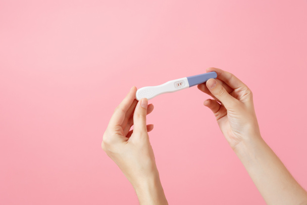 Detailní záběr žena drží v ruce těhotenský test izolované v trendy růžové pozadí. Lékařská zdravotní péče gynekologická, těhotenství plodnost mateřské lidí koncept. Nikdo. Kopírovat reklamní prostor - Fotografie, Obrázek