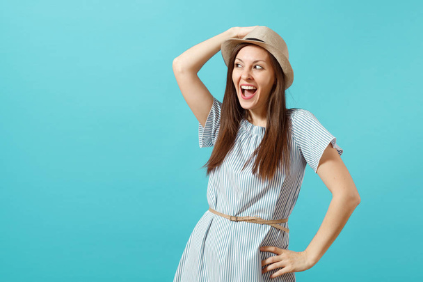 Portrait of excited smiling young elegant woman wearing dress, straw summer hat put hands on head, copy space isolated on blue background. People sincere emotions, lifestyle concept. Advertising area - Φωτογραφία, εικόνα