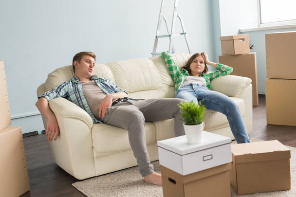Hogar, personas y concepto familiar - Cople joven descansando mientras se muda a un nuevo apartamento
 - Foto, Imagen