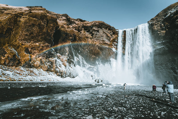 Skogafoss waterfall in Iceland with rainbow on a sunny day with blue sky. - Fotoğraf, Görsel