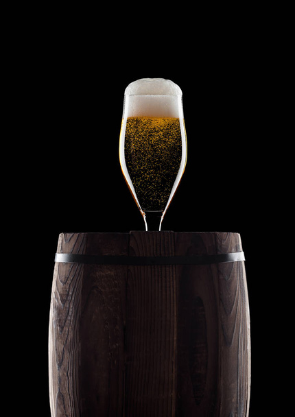 Cold glass of craft beer on old wooden barrel on black background with dew and bubbles - Foto, immagini